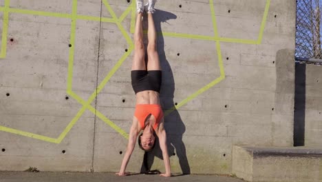 mujer haciendo el pino contra el muro de hormigón al aire libre