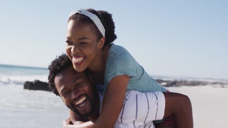 Hombre-Afroamericano-Sonriendo-Y-Llevando-A-Una-Mujer-Afroamericana-A-Cuestas-En-La-Playa