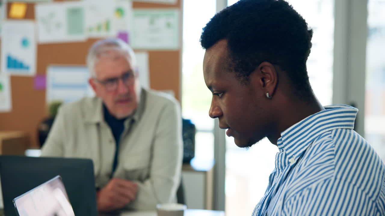 Young Man Focused on Laptop in Office with Colleague