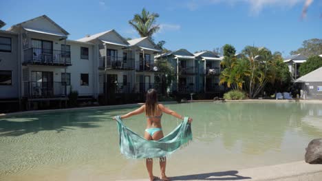 woman poses at the edge of the pool at the front of accommodation structures in noosa lakes resort