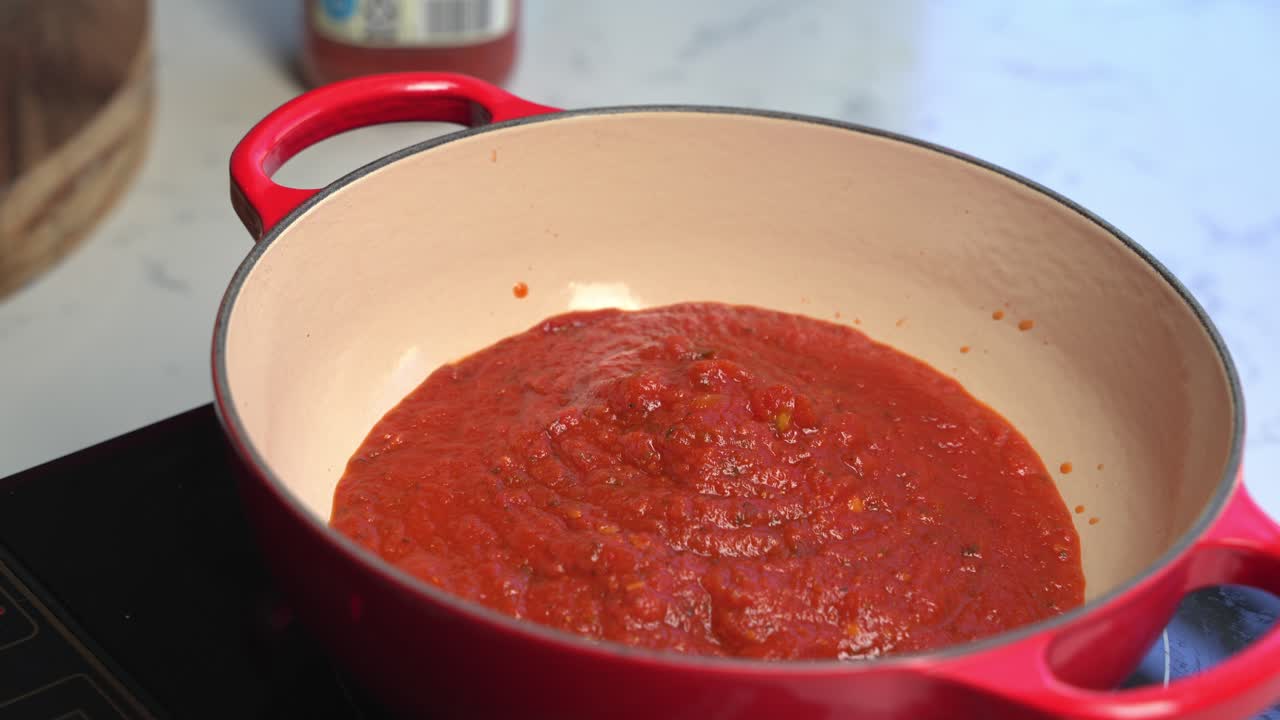Close up view of boiling tomato sauce in kitchen pot, steam rising during cooking process