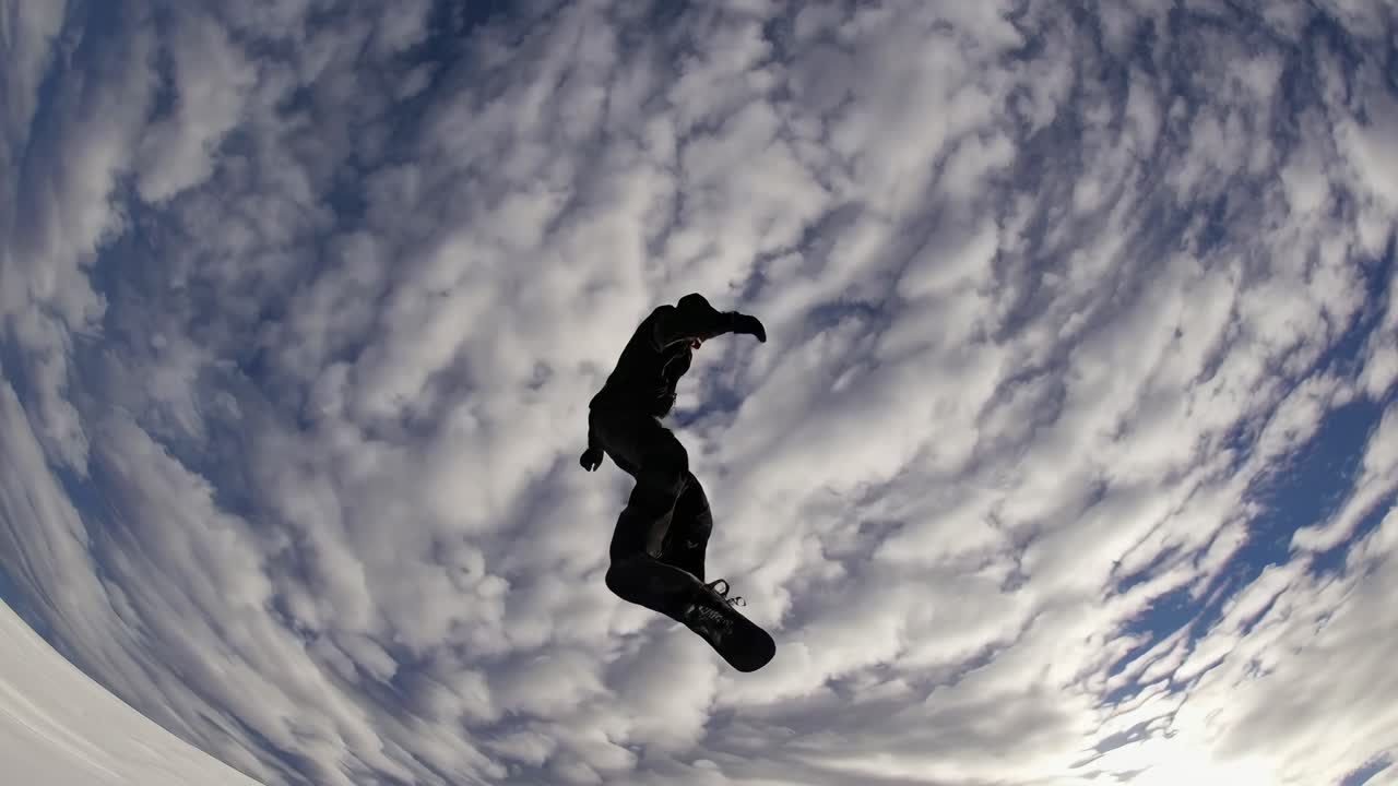 Dynamic low-angle shot of a snowboarder mid-air against a cloudy sky, capturing the thrill