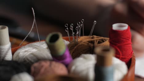 young tailor attaches white textile pieces with sewing pins making reusable face mask at workplace night at home. female hand taking pins from the brown ball of thread. close up