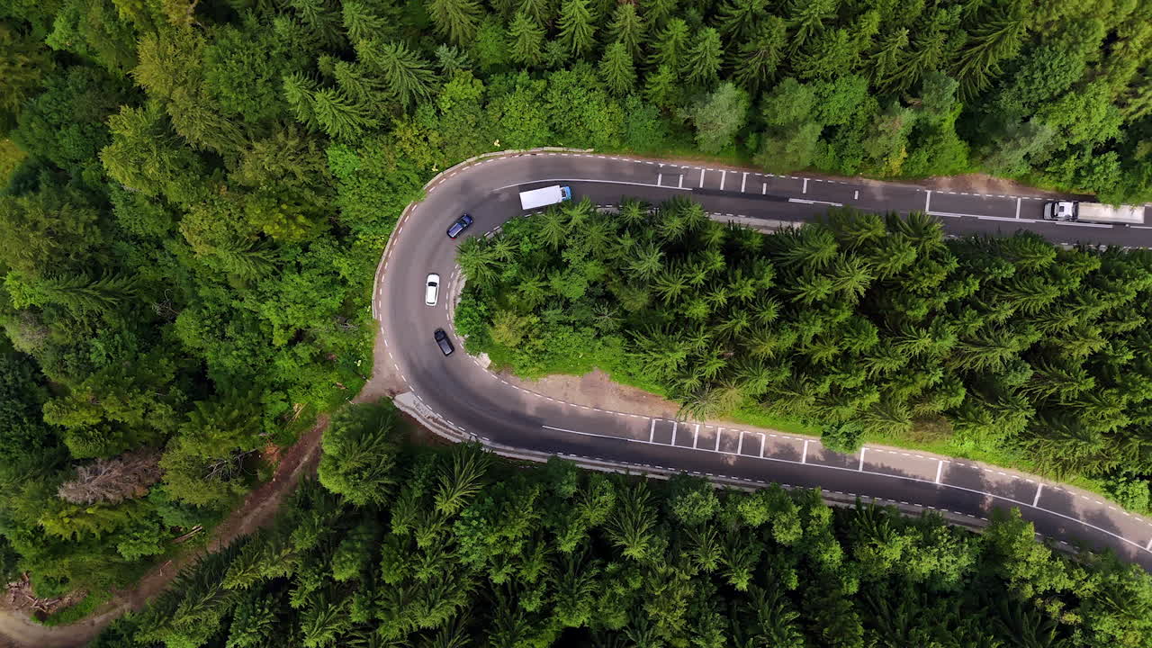 Sharp mountain road turn in green forest, Romania. Aerial top-down view of a sharp road turn surrounded by dense pine forest in the Carpathian Mountains of Romania