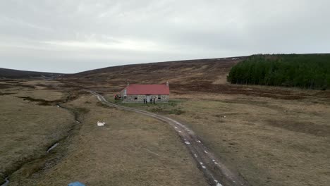 a drone flys over the red house bothy in the scottish highlands as people talk outside the front door