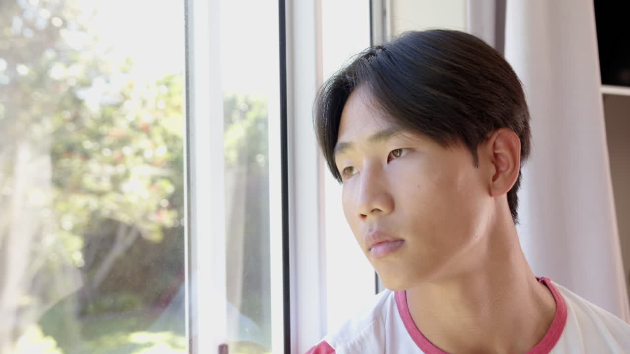 Looking out window, young asian man daydreaming and reflecting in natural light