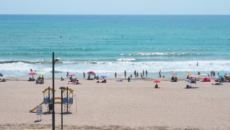 relaxing scene of sunbathers and beachgoers at el campello, costa blanca, alicante, with swimmers enjoying the mediterranean sea close to the beach in spain