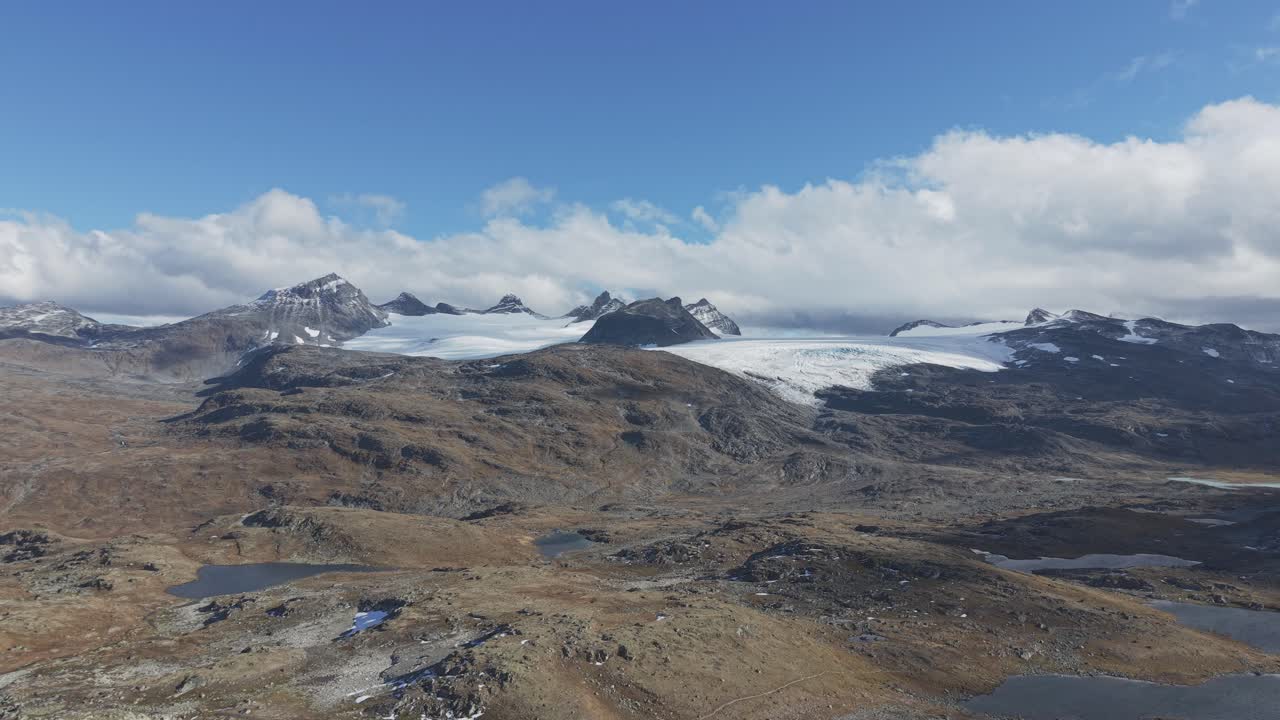 From left to right flying drone footage of beautiful landscape in Jotunheimen National Park with mountains, clouds and glaciers