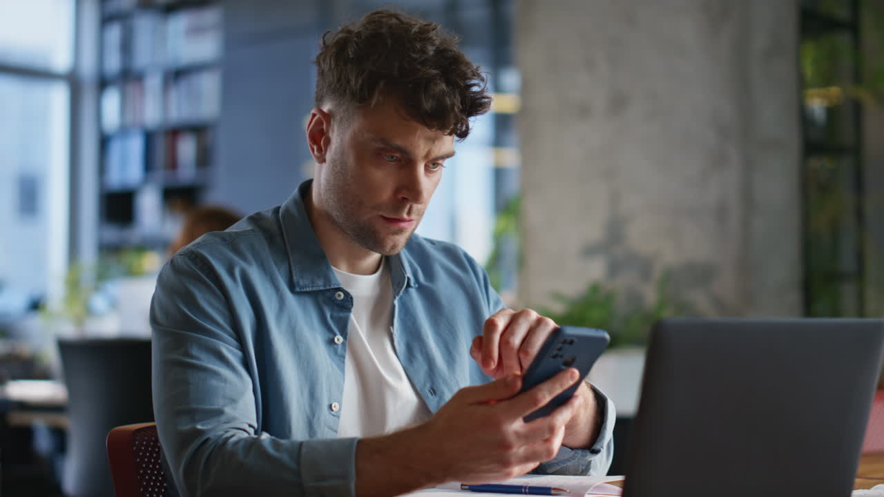 Focused businessman looking smartphone reading messages at laptop table closeup