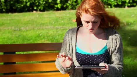 Peaceful-woman-working-with-her-tablet-sitting-on-bench