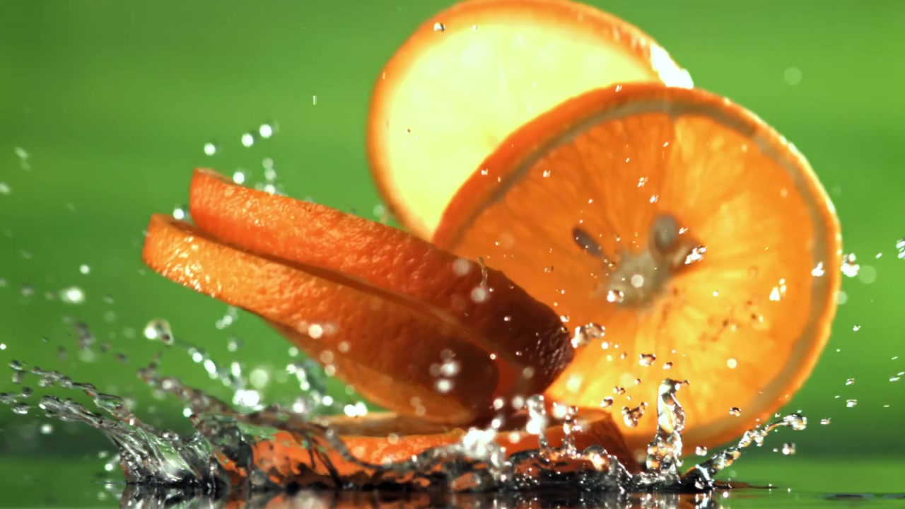 Fette d'arancia fresche che schizzano nell'acqua su sfondo verde