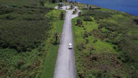 tilt up drone shot of a white car driving along banzai cliff at tinian island