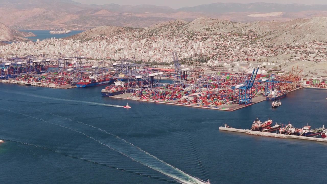 Beautiful aerial view of a tugboat navigating towards the commercial harbor of Piraeus. Showing cargo ships. Cranes. And stacked containers ready for international shipping and freight transportation