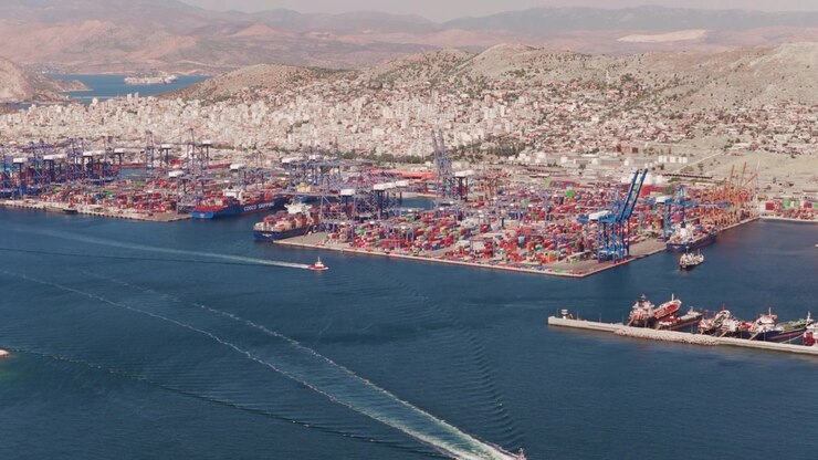 Beautiful aerial view of a tugboat navigating towards the commercial harbor of Piraeus. Showing cargo ships. Cranes. And stacked containers ready for international shipping and freight transportation