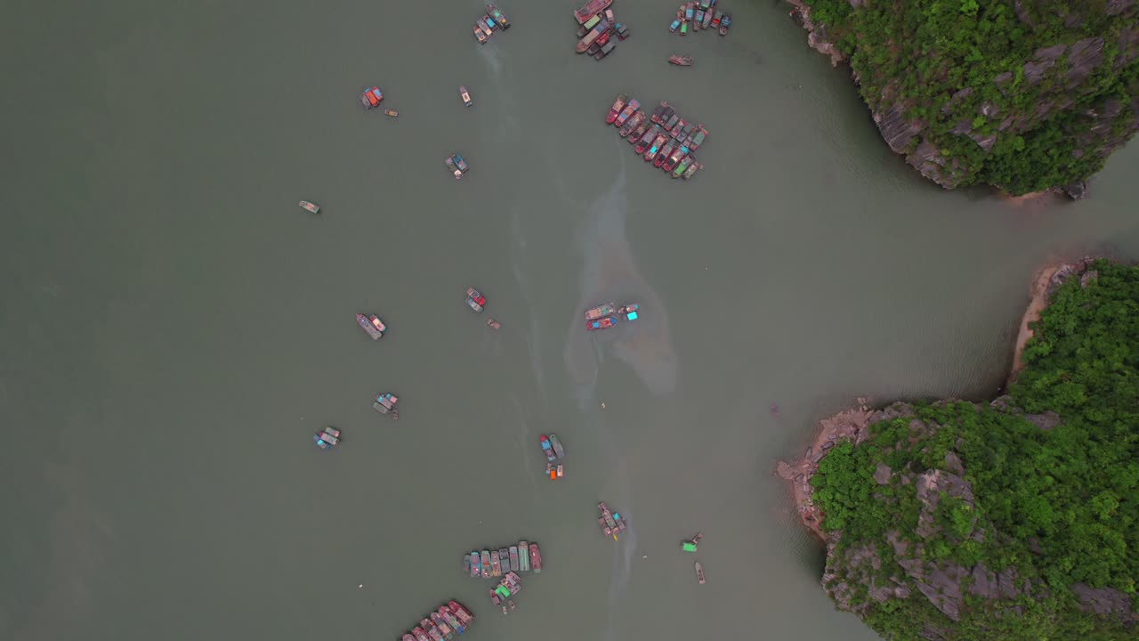 Aerial - boats scattered on calm waters of Halong Bay, surrounded by lush cliffs. Vietnam