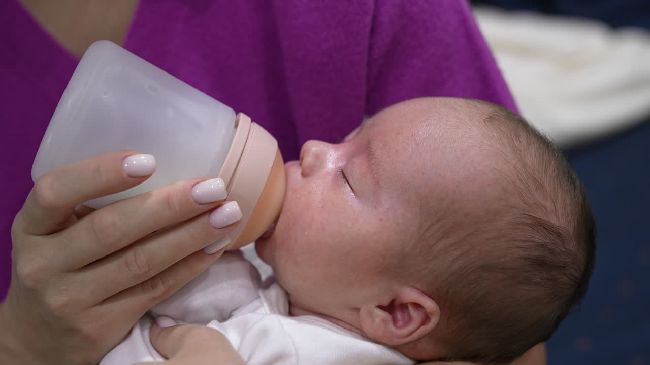 Loving mother holding a baby in her arms and feeding it from the bottle. Newborn child being fed from a bottle with pacifier. Close up.