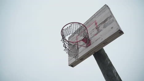 old basketball hoop with torn net hanging in wind and peeled off paint