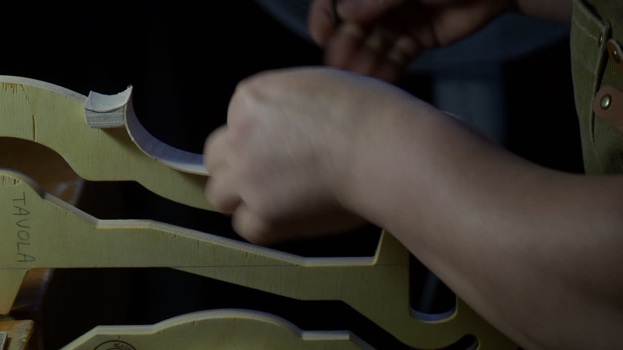 Violin rib edge being shaped on internal mold by luthier hand, refining curve and outline of new instrument body with controlled movement in traditional workshop environment, extreme close up shot