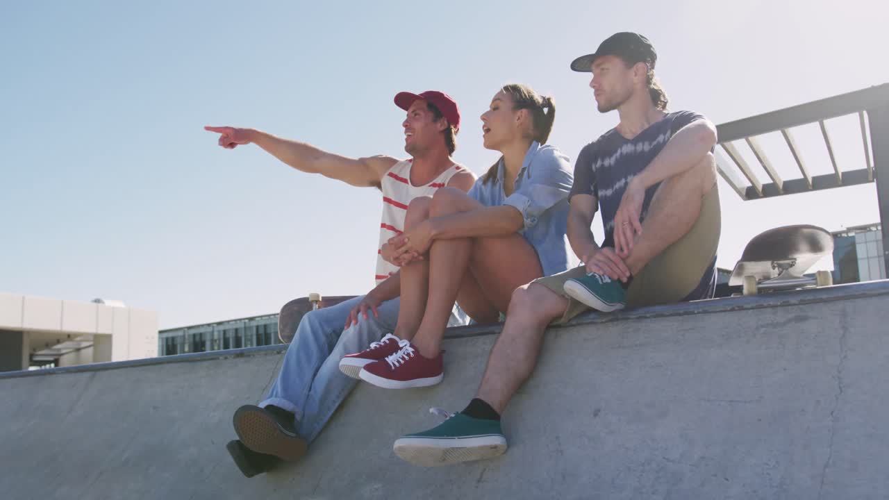 mujer caucásica y dos amigos masculinos sentados hablando y señalando algo en la distancia en un día soleado