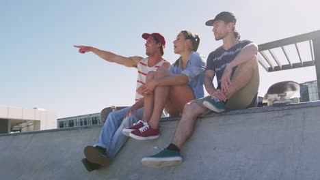 caucasian woman and two male friends sitting talking and pointing something in distance on sunny day