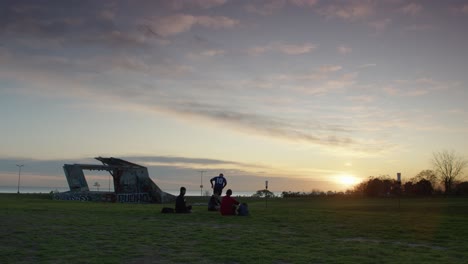 friends play football soccer at sunset in a grassy park near graffiti-covered ruins by the sea