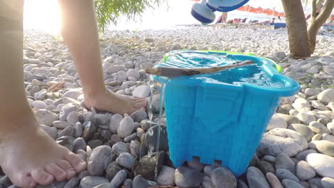 Kleinkind-Am-Strand,-Der-Einen-Blauen-Spielzeugeimer-Mit-Atoy-bewässerungstopf-In-Der-Nähe-Füllt