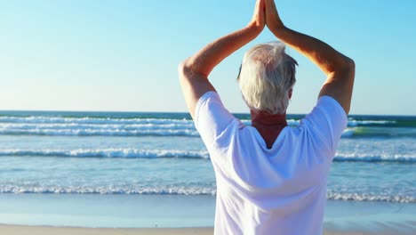 senior man doing yoga on the beach