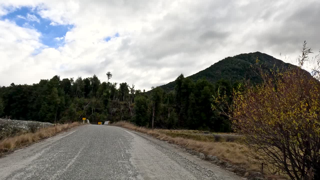 Vehicle travels gravel road through scenic Glenorchy valley, overcast daylight, wide angle, steady movement