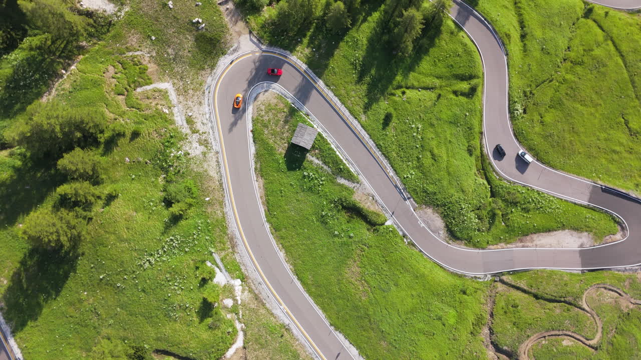Drone top view of two sports cars driving along a winding mountain road surrounded by forest and fields. Category: Transportation