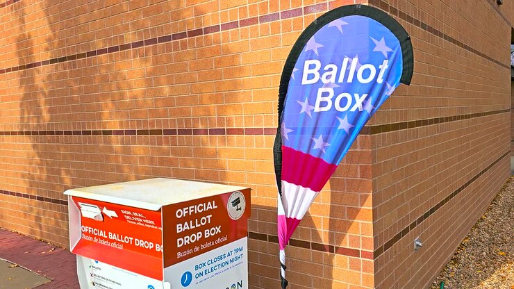 Una grande cassetta postale in metallo, etichettata come “Official Ballot Drop Box” in inglese e “Buzón de Boleta Oficial” in spagnolo, fornisce agli elettori un luogo sicuro e ufficiale in cui consegnare le schede elettorali compilate.