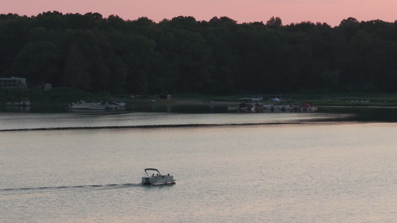 Telephoto aerial panning shot of a pontoon boat on a lake during sunset in Center City, Minnesota. 4K