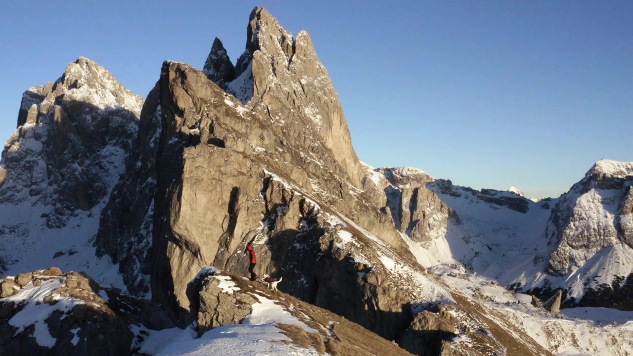 Ripresa con drone di un escursionista e un cane davanti alla cresta del Seceda, inverno nelle Dolomiti, Italia