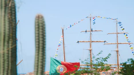 tall ship with portugal colours flying and various smaller signal flags while docked in curaçao