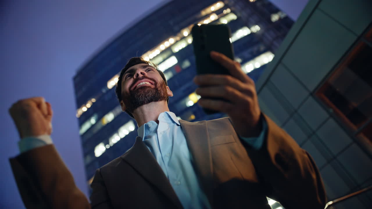 Business winner reading smartphone notification rejoicing at evening low angle