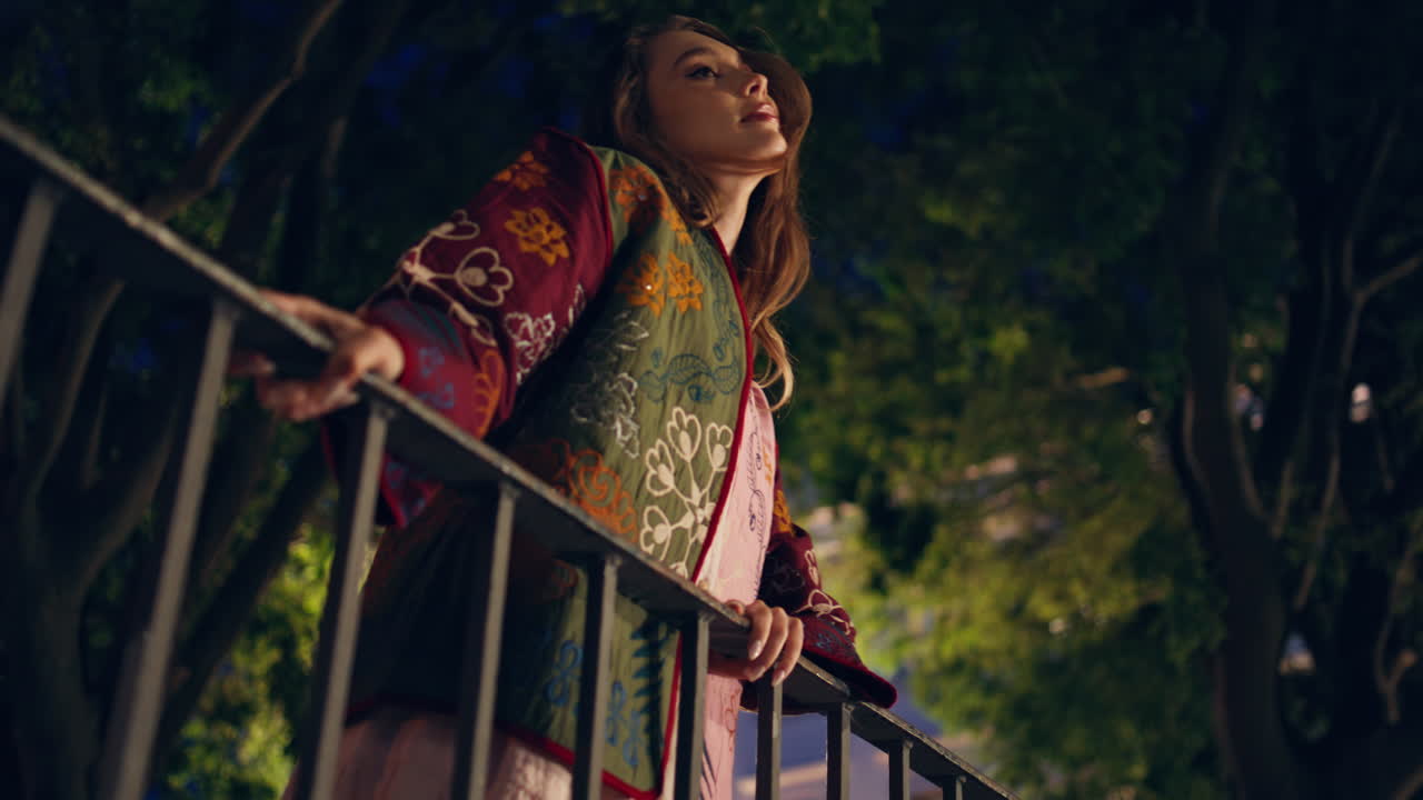 밤 공원에서 편안한 여자가 레일링에 기대어 행복한 소녀가 황혼에 정원을 포즈하고 있습니다.