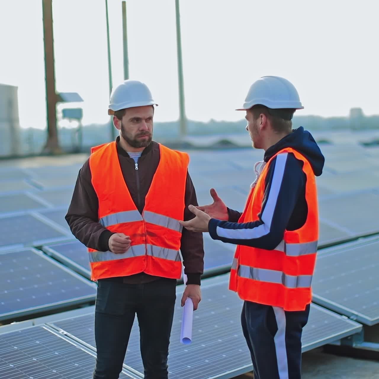 Installing photovoltaic panels. Workers in orange uniform and hardhats on solar farm background. Engineers are talking among solar panels.