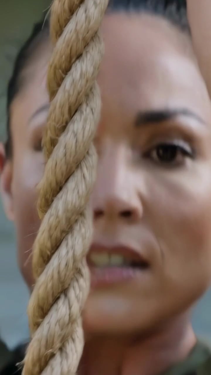 Video verticale: Una donna con un top mimetico che tira e si sforza su una corda durante un allenamento in palestra per la forza.