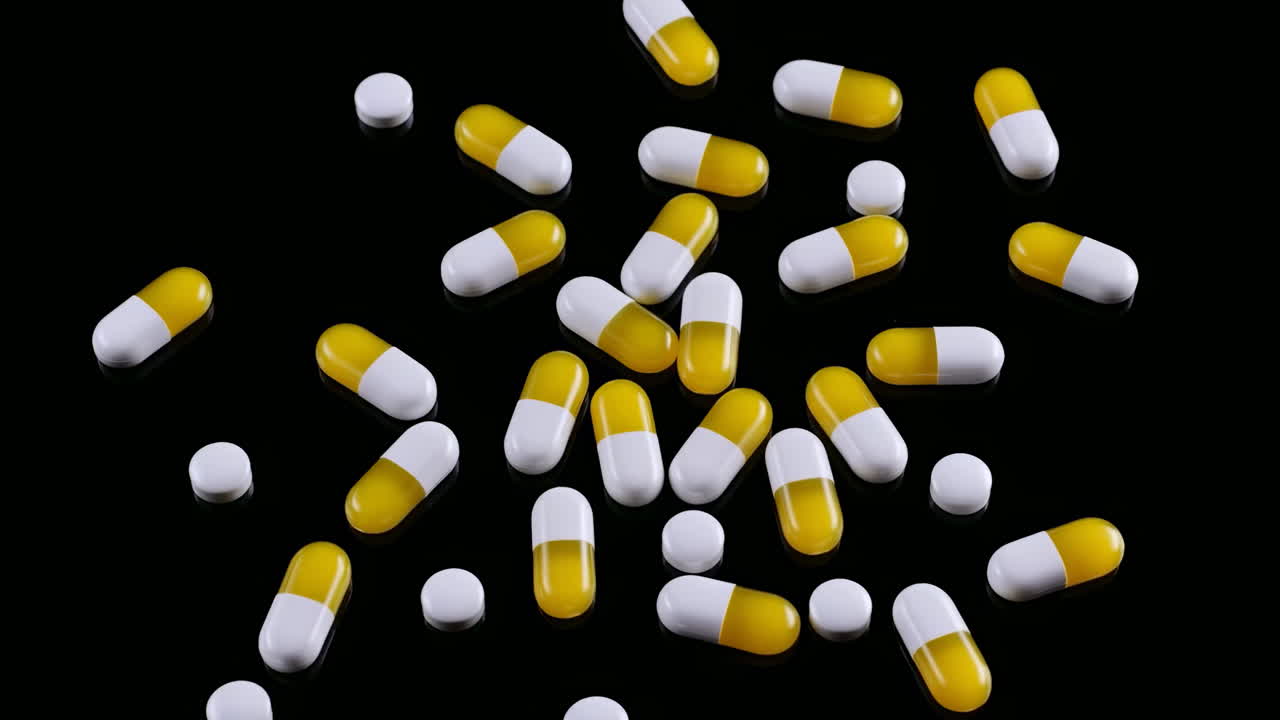 Capsule giallo-bianche sparse su sfondo nero, primo piano che mostra capsule lucide bicolore che rotolano