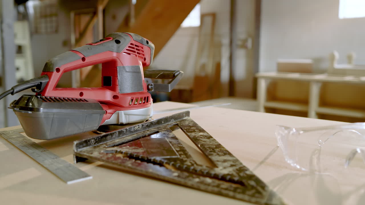 African American craftsman entering shop holding tablet, glancing at sander, square on bench