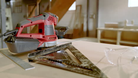 african american craftsman entering shop holding tablet, glancing at sander, square on bench