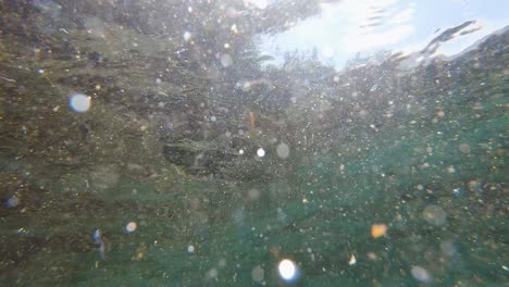 sumérgete en la luz del sol debajo de la superficie ondulada del lago turquesa claro, bajo el agua con un amplio pedestal hacia abajo