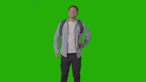 retrato de tres cuartos de longitud de un estudiante universitario o universitario masculino sonriente con una computadora portátil contra una pantalla verde
