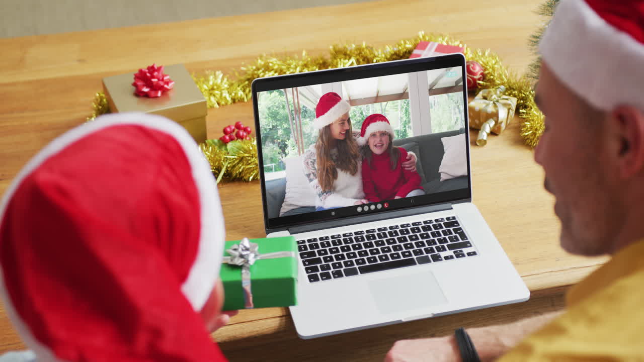 padre y hijo caucásicos con sombreros de santa usando una computadora portátil para una videollamada de navidad con la familia en la pantalla