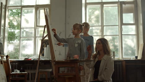 joven maestro de arte sentado cerca del caballete con los niños