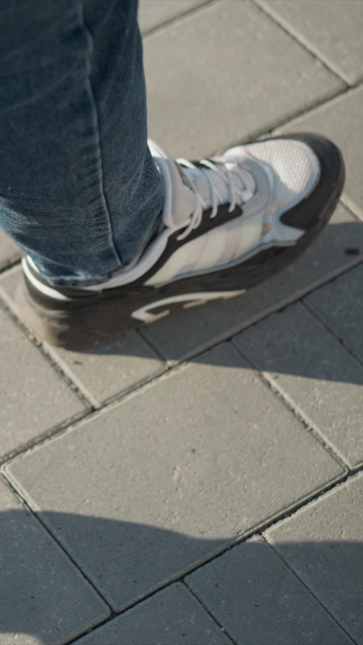 Close up of person foot in white sneakers walking on gray brick pavement. focus remains consistently low angle capturing movement and texture details like shoe laces and concrete surface