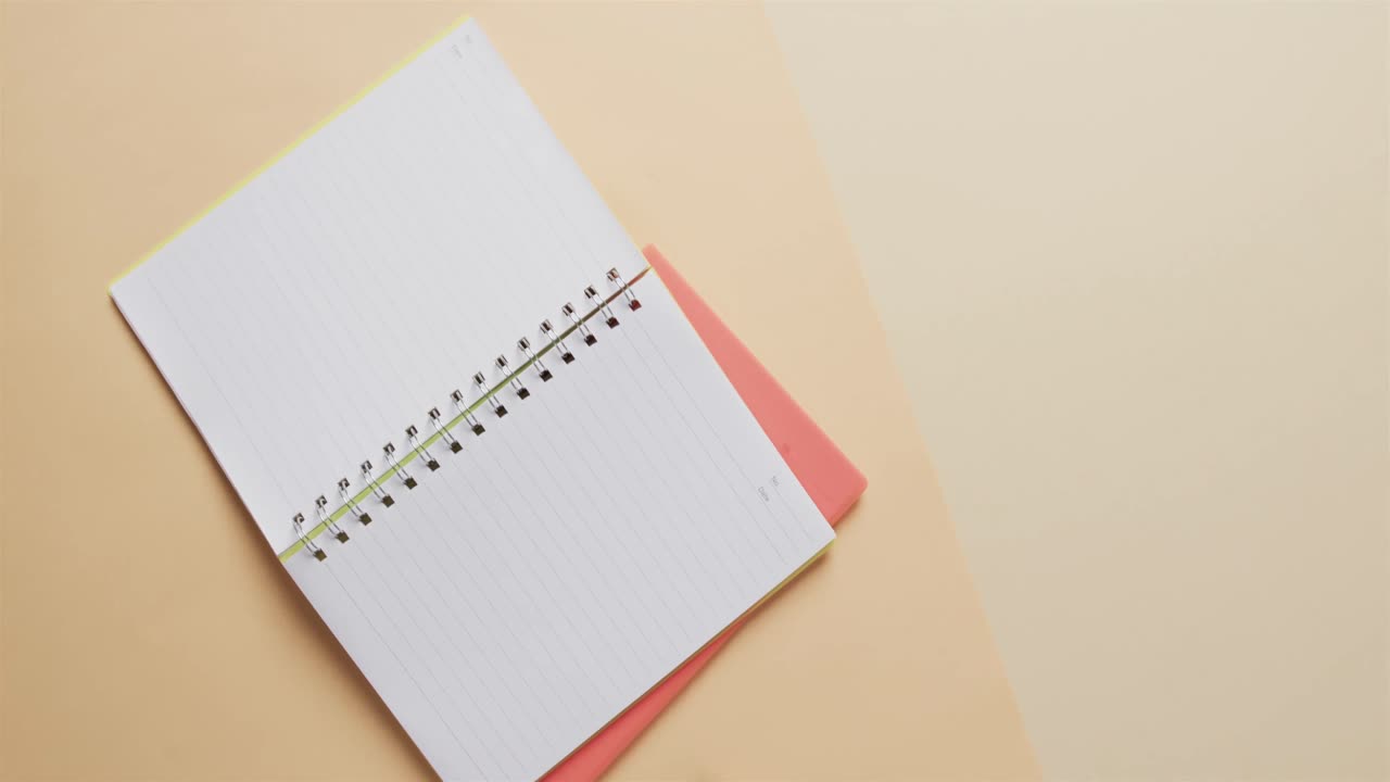 Overhead view of open notebook with pink marker with copy space on beige background, in slow motion