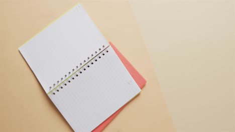 overhead view of open notebook with pink marker with copy space on beige background, in slow motion