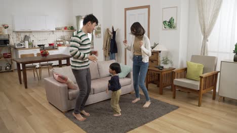 slow motion with full length cheerful asian father, mother and preschool boy enjoying dancing to music in the living room at home