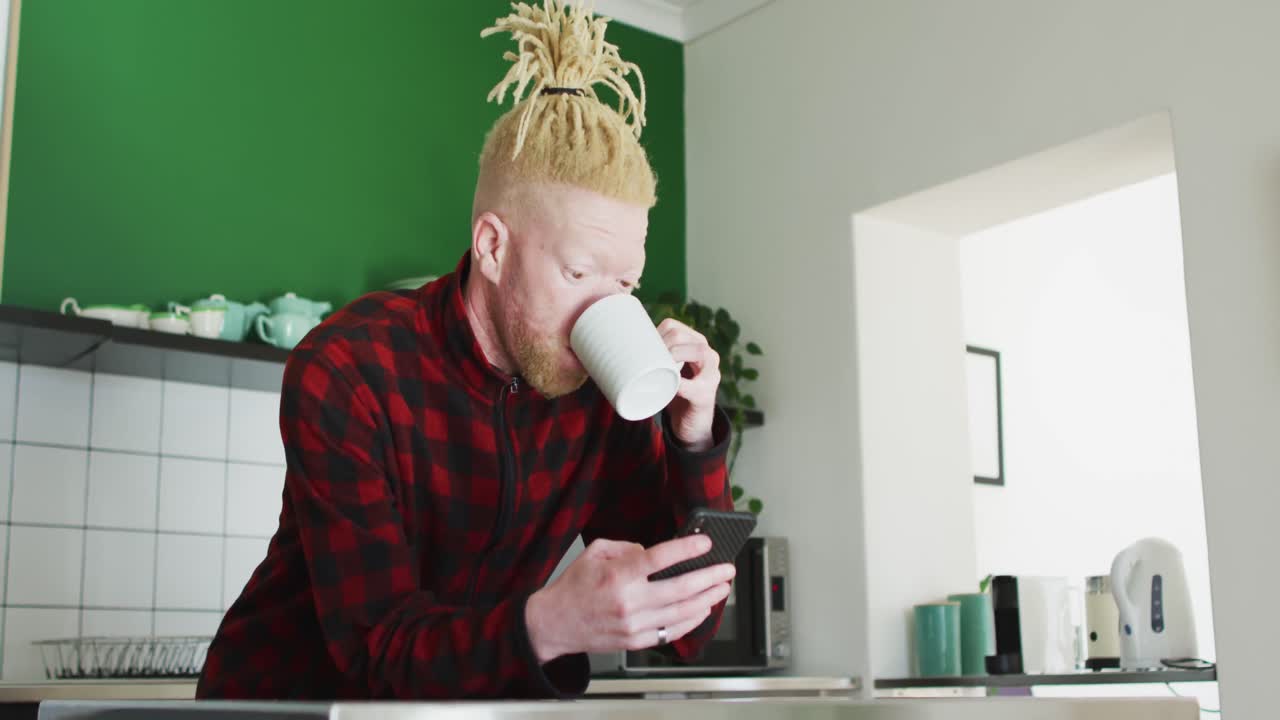 hombre albino afroamericano pensativo con rastas usando un teléfono inteligente y bebiendo café