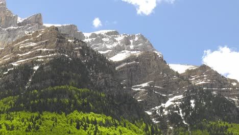 snowy mountain range with clouds building in blue sky, pan shot